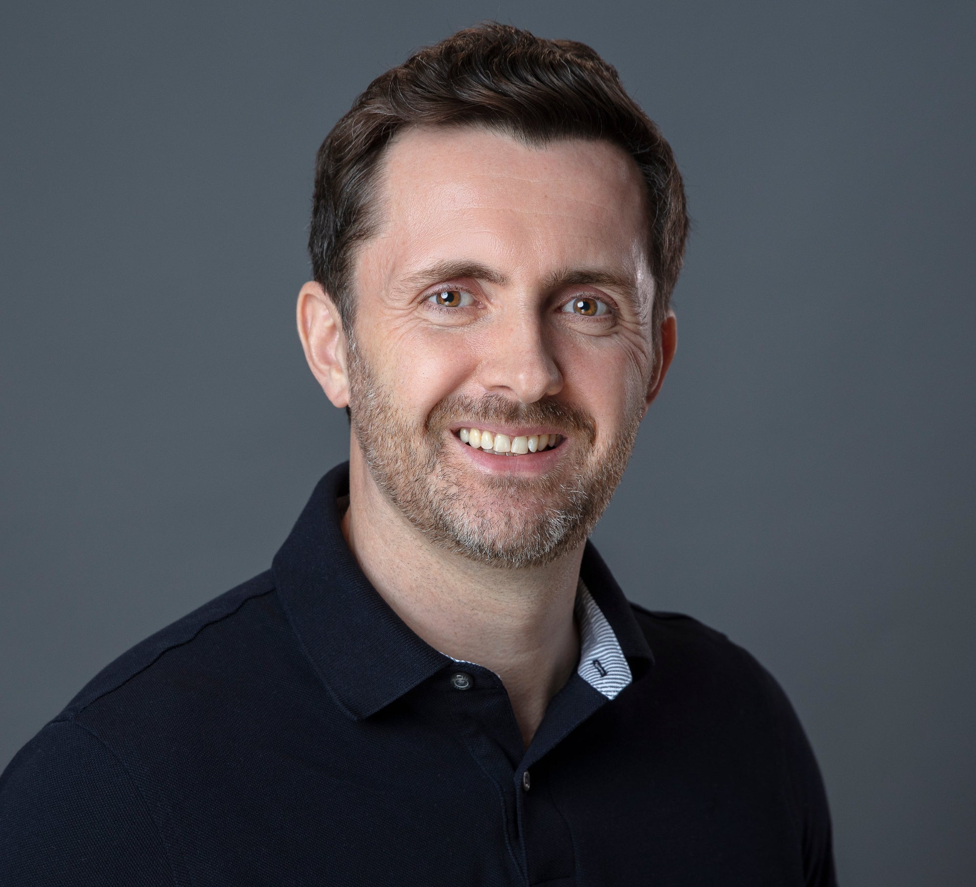 Albert wearing a dark polo shirt against a gray background