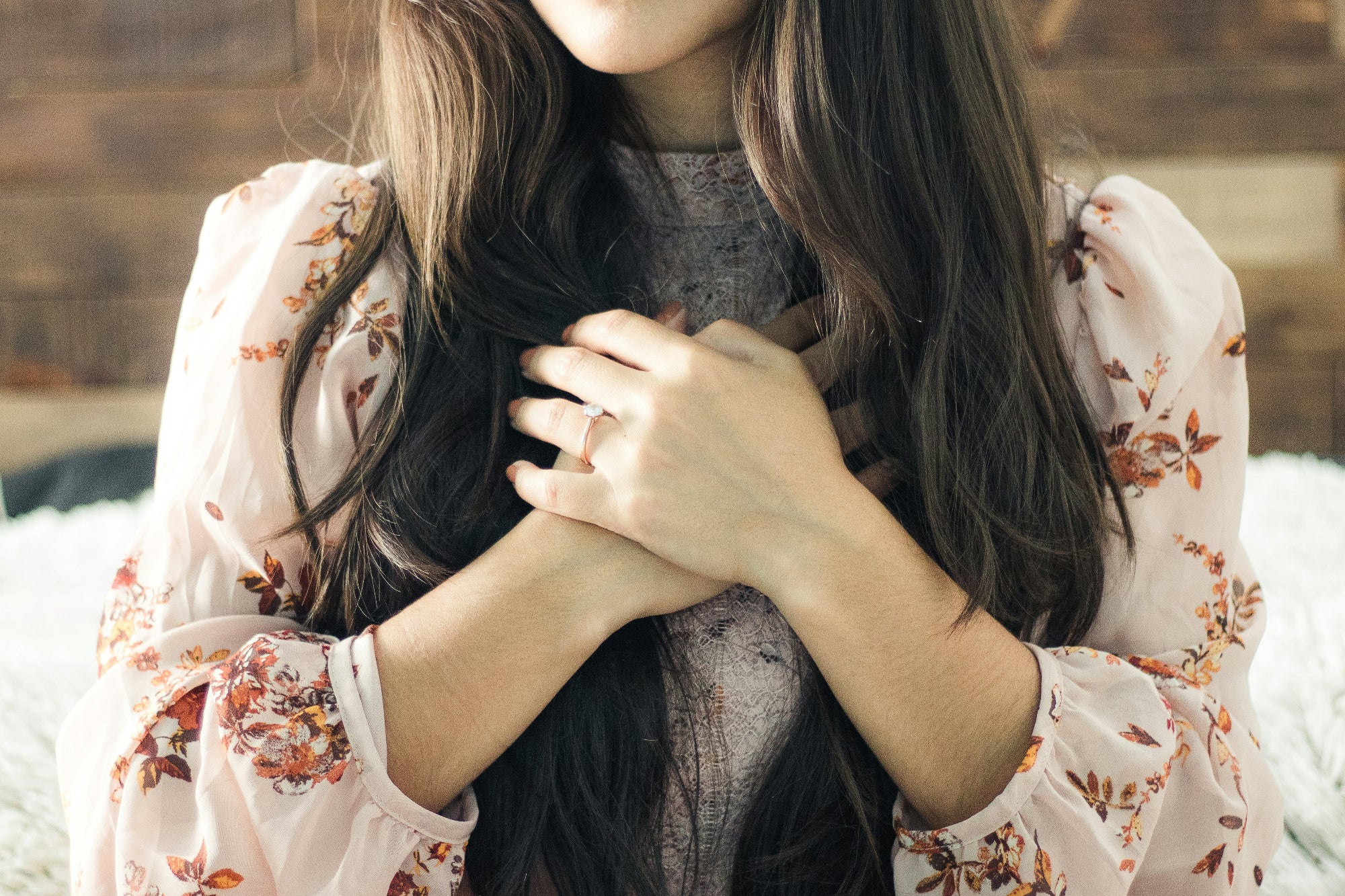 Woman with long dark hair wearing a floral blouse sitting on a soft surface.
